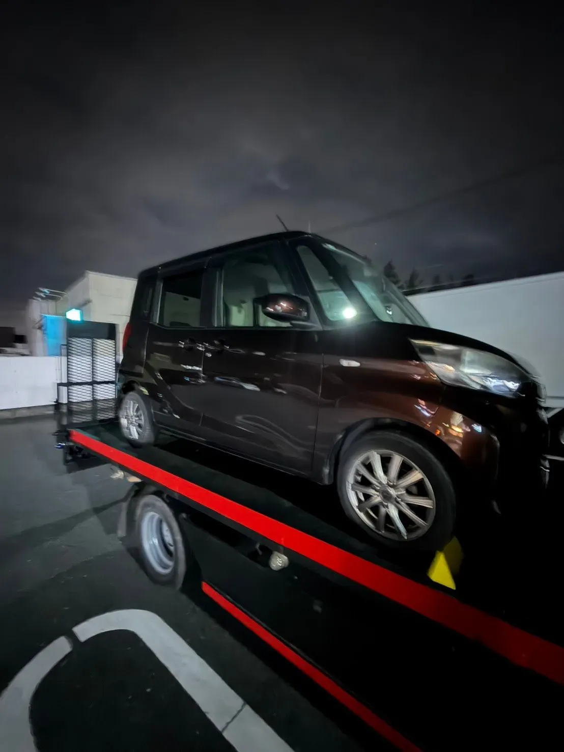 積載車に載せた軽自動車。前輪に黄色い輪止めをかけている